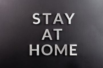 the words stay at home laid with silver metal letters on matte black background in flat lay...