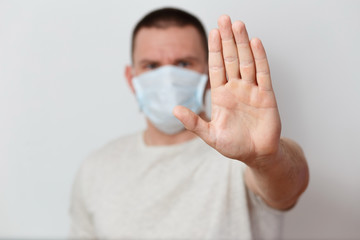 a brutal, middle-aged man in a medical mask on his face with his palm outstretched on a white background. stay at home