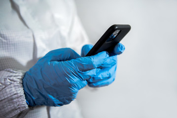 Man wearing a protective suit and blue gloves using smartphone on laboratory.