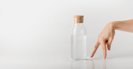 A walking finger man moves toward a glass bottle of clear water.
