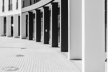 Semicircle shape colonnade. Entrance to modern building. White and dark grey pillars in a sunny day. Black and white picture.