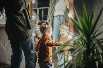 little attractive girl of 2 years is playing near the mirror next to her mom who is applying...