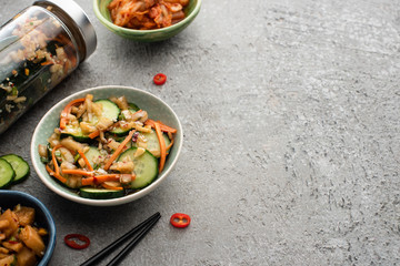 tasty kimchi in bowls and jars near chopsticks on concrete surface