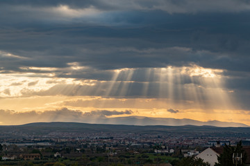 Dramatic sun ray through low clouds over city at sunset. The sun cuts through the clouds over the city. Sunbeams on the city