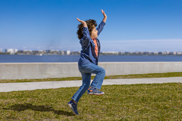 Fototapeta premium An excited little boy hops and skips in the air, arms and legs up along the waterfront.