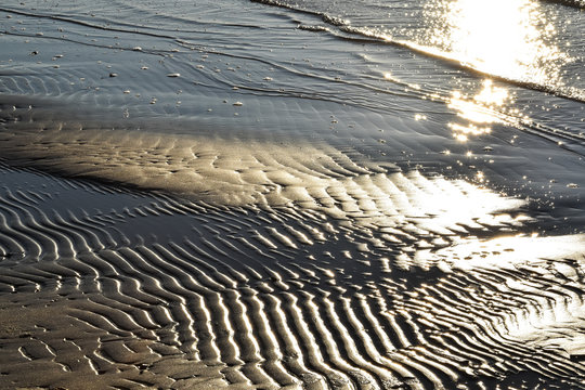Shiny wet sand on the beach reflecting golden sunset