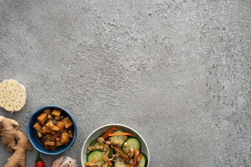 top view of tasty kimchi in bowls near ginger and sliced garlic on concrete surface