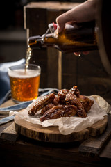 beer pouring into glass and fried chicken wings with sesame seeds on wooden background