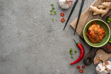 top view of bowl with kimchi on cutting board near chopsticks, ginger, chili pepper and garlic on...