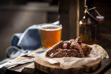 Chicken wings with sesame seeds and glass of beer with bottle on wooden background