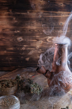 steaming bong. open grinder with marijuana. cannabis on a wooden surface. on a wooden tray stained with paint.