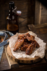 Chicken wings with sesame seeds and glass of beer with bottle on wooden background