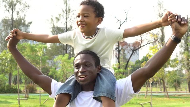 Happy African American father and son piggyback in outdoor park. Fatherhood and family lifestyle concept