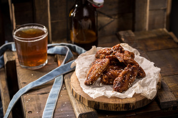 Chicken wings with sesame seeds and glass of beer with bottle on wooden background