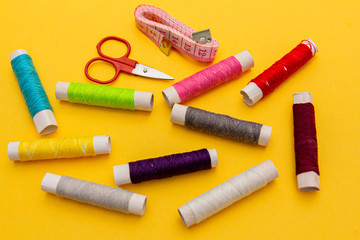 Fototapeta na wymiar Thread, needles, scissors and meter yellow background. tailoring set. sewing kit multi-colored