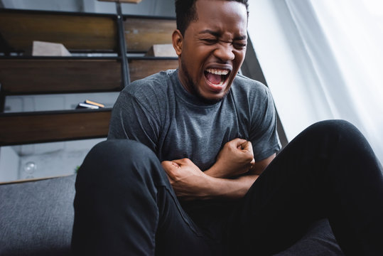 stressed african american man screaming while having panic attack at home