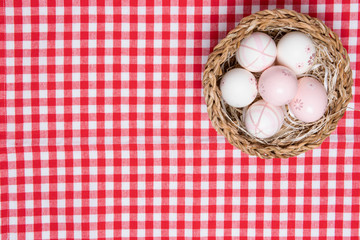 Easter eggs background. Top view on a wicker basket with colorful easter eggs on a red tablecloth or napkin. Decoration background with space for product display montage. Happy Spring card template.