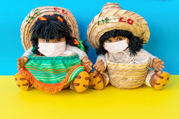 Figures of a boy and a girl in sombrero in protective medical masks on the background of the sea. Coronovirus and travel concept.