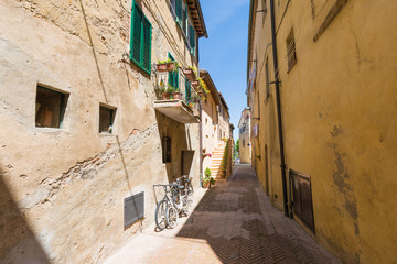 Fototapeta na wymiar Beautiful Italian street during summer or spring season of a small old provincial town. Picturesque corner of a quaint hill town Tuscany Italy. Coronavirus impact, empty street. Travel background