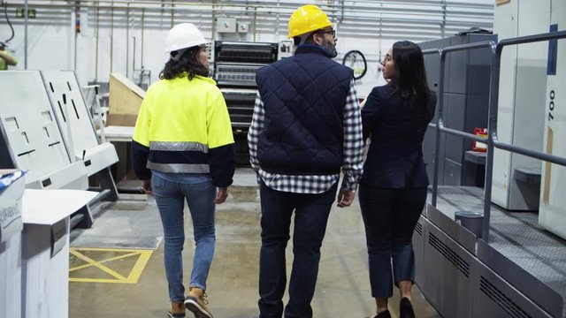 Back view of HR specialist showing factory to new technicians. Rear view of project manager and engineers walking at printing house. Industry concept