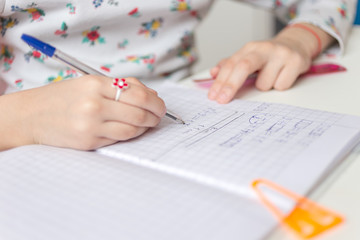 Close up of a girl writing math exercise at home. Selected focus.