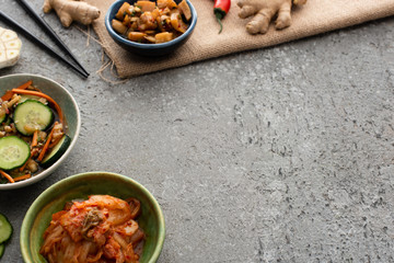 selective focus of bowls with kimchi near chopsticks and ginger on concrete surface