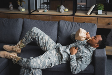 african american soldier in military uniform holding paper bag while having panic attack  at home