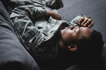 Tired African American soldier in military uniform sleeping in sofa at home