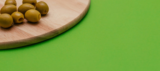 Green pitted olives lie on a round wooden cutting board on a green background closeup.Harvest coronavirus concept 2020.Agricultural crisis linked to the coronavirus pandemic.Copy space,selective focus