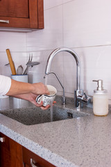 Household chores. A woman washes dishes on the background of kitchen utensils, water flows from the tap.