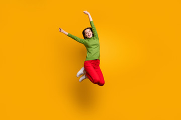 Full body photo of positive funky girl have winter holidays jump raise her hands feel content emotions wear casual style outfit isolated over yellow color background
