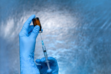 the hands in blue gloves hold a glass bottle with a vaccine and a syringe with a needle for...