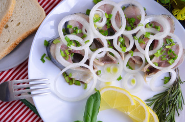 Herring fillet with salt, pepper, herbs, onion and lemon on black plate on white background. top view. healthy food
