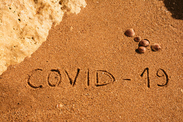 Fototapeta na wymiar Travel and tourism concept, novel coronavirus 2019-nCoV pandemic alert. COVID-19 text written on the sandy beach in Algarve. The spread of corona virus in the World impact on tourism and holidays.