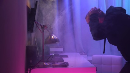 A frightened young man in hoodie runs up to burning laptop. Smoke is coming from computer and man...