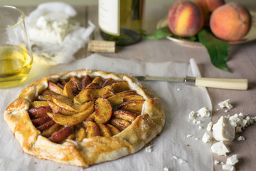 Fresh peach crostata on parchment paper with feta cheese, white wine and peaches. 