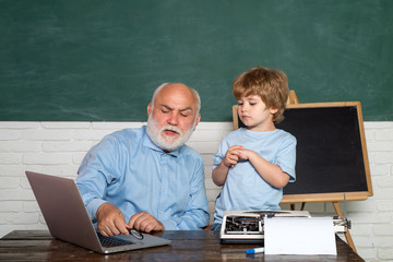 Man teaches child. Grandfather and grandson. A grandfather and a toddler are working with notebook. Back to school. Student. Happy Pupil with over blackboard background.