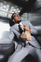 scared african american businessman with paper bag suffering from panic attack in elevator