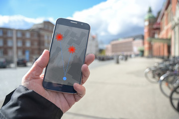 Hand with mobile phone and coronavirus tracking  app against the spread of the pandemic, but controversial when it comes to protection of personal data, blurry city background with copy space