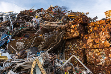 Cubes of rusty cans pressed and stacked next to other scrap in a scrap yard.