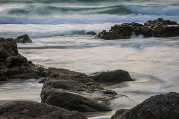 Long Exposure Shot of Rocks on a Beach with Ocean Waves during Daylight