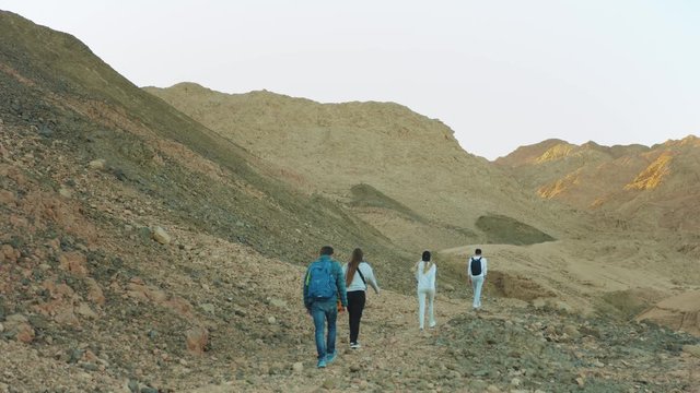 Group of tourist walk along the rock canyon in hot desert, tourists take picture and have fun. Desert mountains background, Egypt, Sinai, slow motion, 4k
