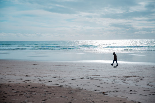 Silhouette of a Lonely Man on a Sandy Beach with Blue Sky and Clouds