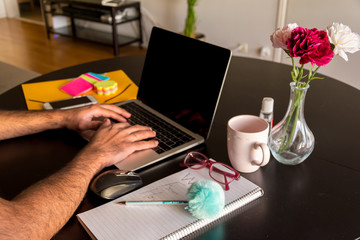Working from home concept with male hand typing on a laptop keypad with coffee cup, mouse and notepad on a dining table