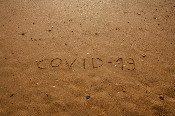 Travel and tourism concept, novel coronavirus 2019-nCoV pandemic alert. COVID-19 text written on the sandy beach in Algarve. The spread of corona virus in the World impact on tourism and holidays.
