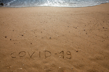 Concept of coronavirus holiday, travel and tourism. MERS-Cov. 2019-nCoV. COVID-19 text on the sandy beach, coast and ocean in the background.