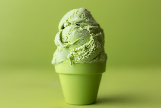 Matcha flavored ice cream in a matching green cup against a tea green background. Copy space. 