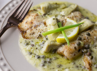 Close up view of fish piccata made with tilapia, capers, and artichokes in a creamy lemon sauce. 