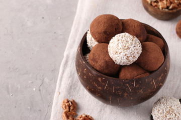 Energy balls of nuts and oatmeals with coconut flakes and cocoa in coconut bowl on gray background, horizontal format, Copy space
