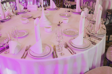 Elegant white bridal dinner. Tables set for an event party or wedding reception. Purple lights and decorations for a party event or gala dinner with color lamps.